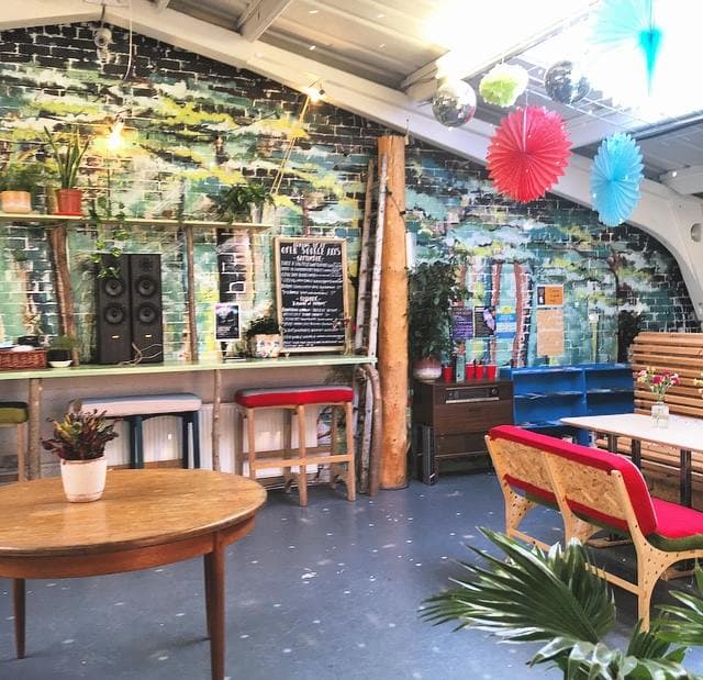 The cafe space with a chalkboard menu above the bar, stools, tables and a painted brick mural.