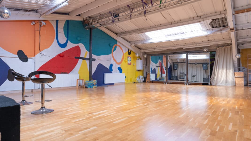 View of our upstairs, dance floor studio, with a painted wall and movvable mirrors in the background. 2 chairs are to the left as if at the front of a stage
