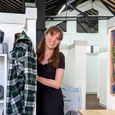 A smiling person beside a checked shirt and white studio partitions.