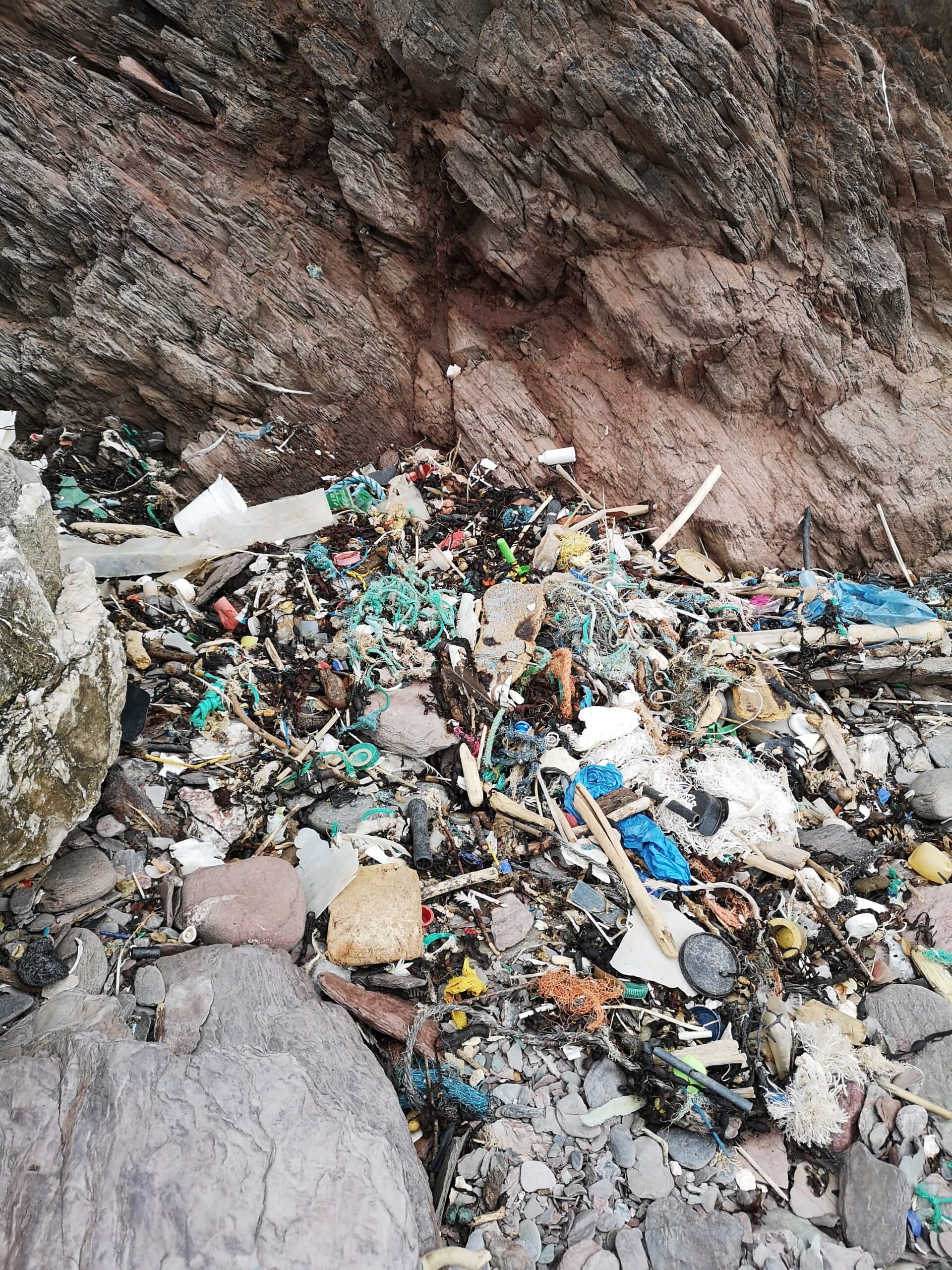 an image showing lots of pieces of plastic and litter on the beach between rocks