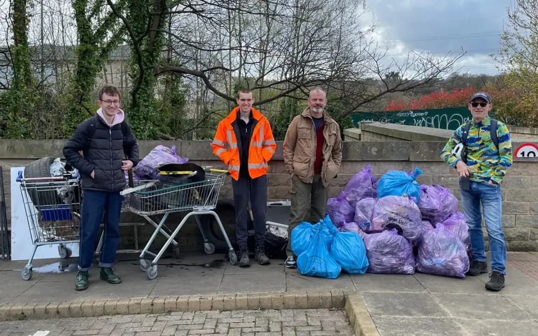 Image showing people who have collected litter. There is a large pile of blue bags containing litter and a trolley that has been removed from the local woodland