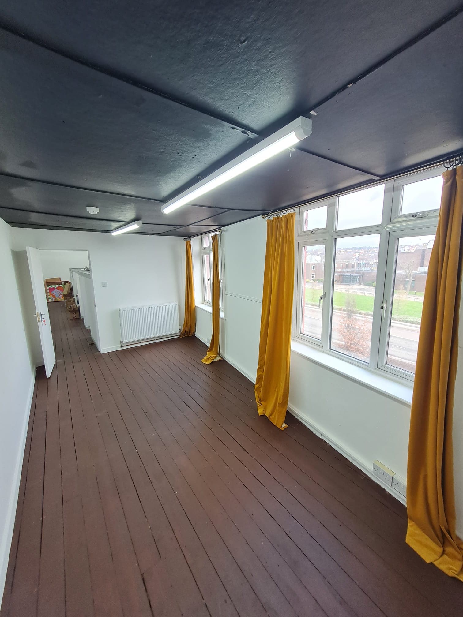 well lit empty lockable studio room, with brown wooden floorboards and yellow curtains that reach all the way to the floor