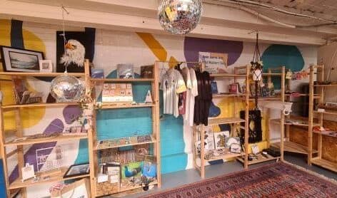 The Maker Shop: wooden shelves of handmade goods and prints in front of a painted mural.