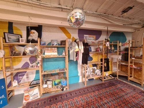 colourful mural behind open wooden open shelves, with a variety of handmade gifts and items