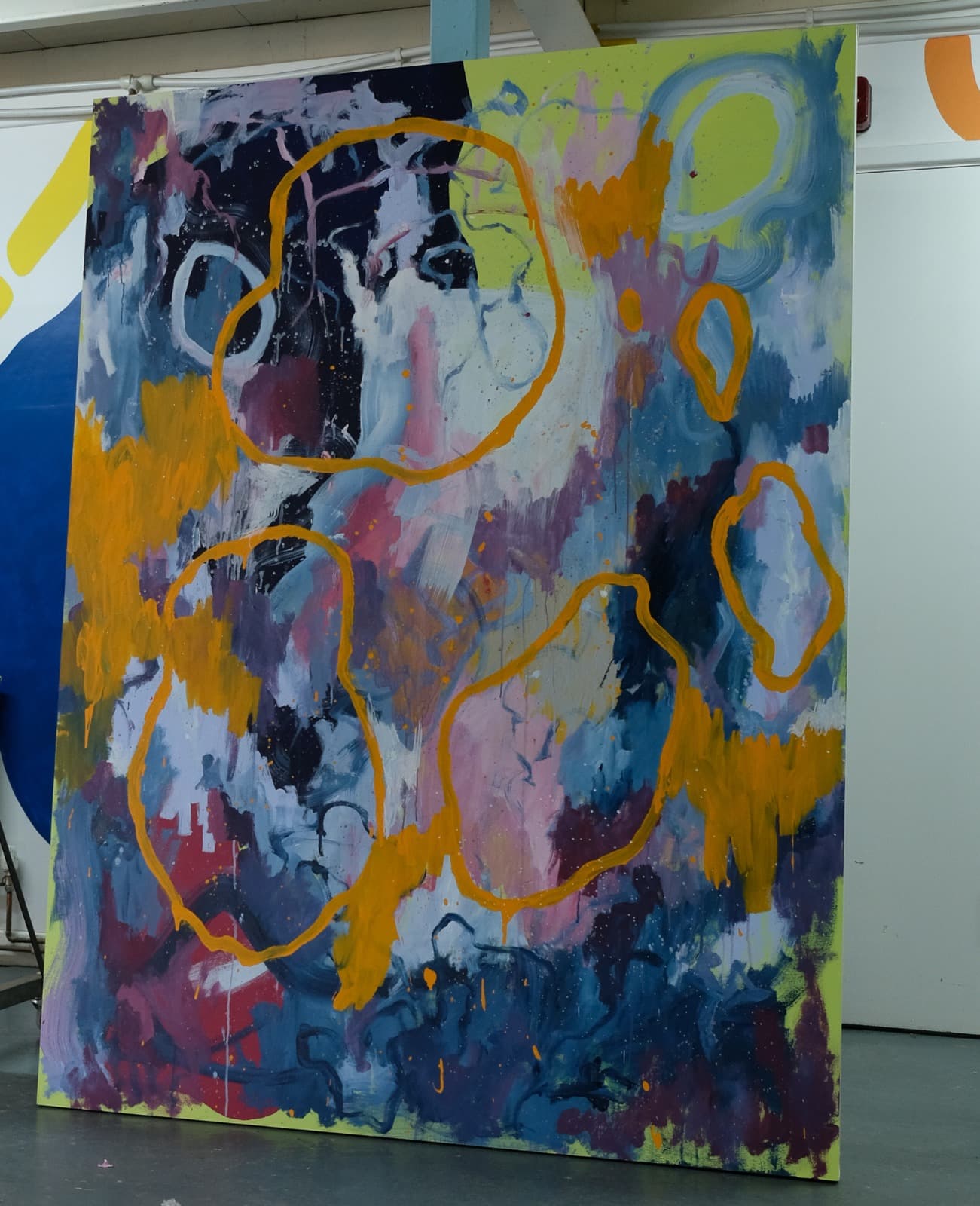 A large abstract painting on display by Niko. The canvas features bold swirls and splashes of color—deep blues, purples, and pinks—overlaid with looping orange outlines. The style is expressive and gestural, giving the impression of cosmic or organic forms.