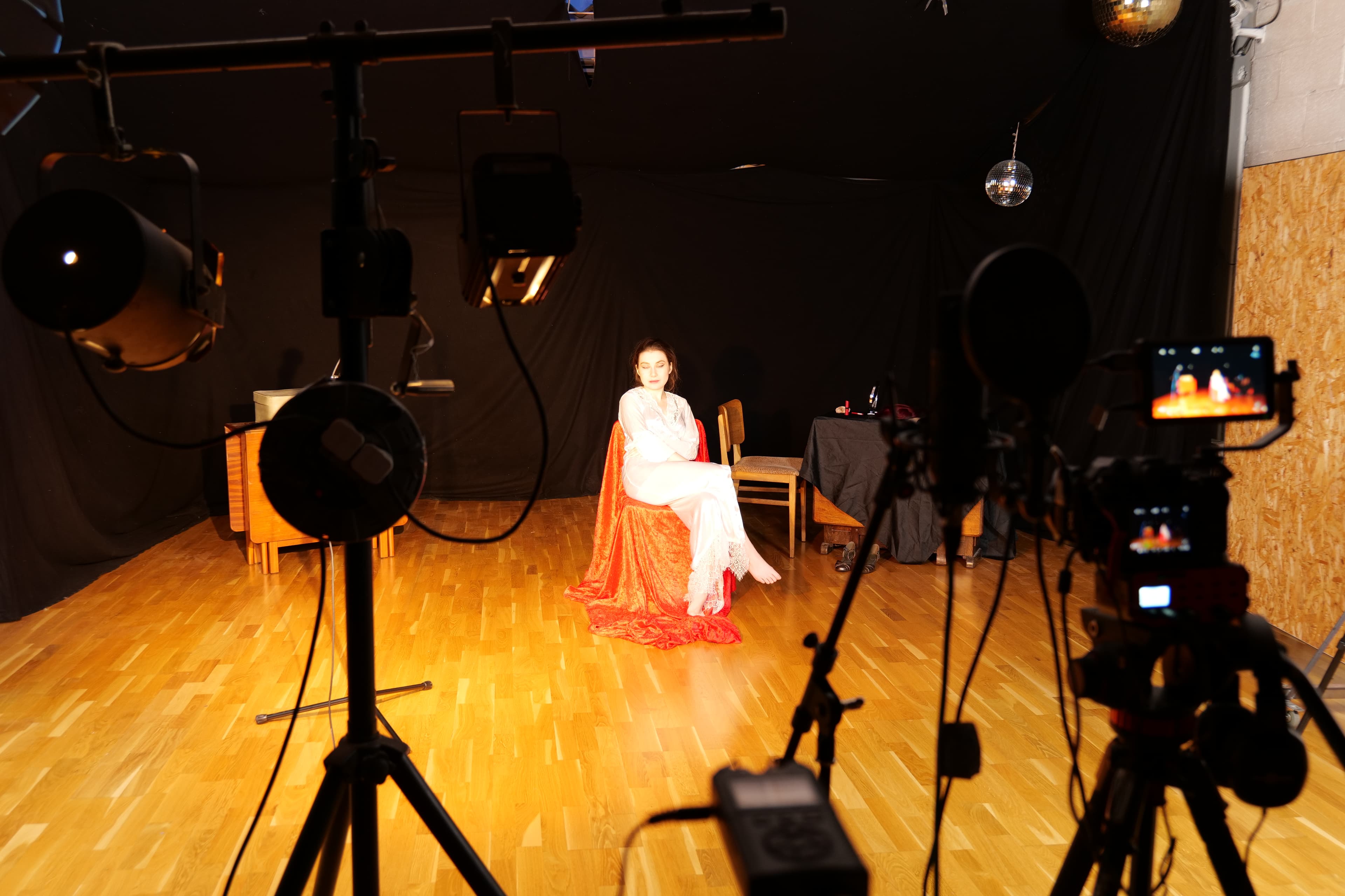 A performer in white filmed on the dance floor, surrounded by studio lights, cameras and mirror balls.