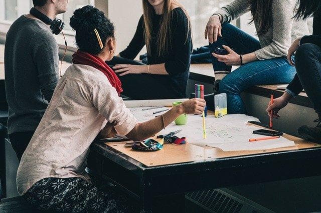 Five young people around a table with felt pens and large sheets of paper, planning together.