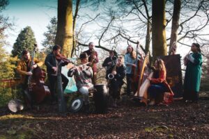 a large band of abut 11 musicians play in a woodland scene