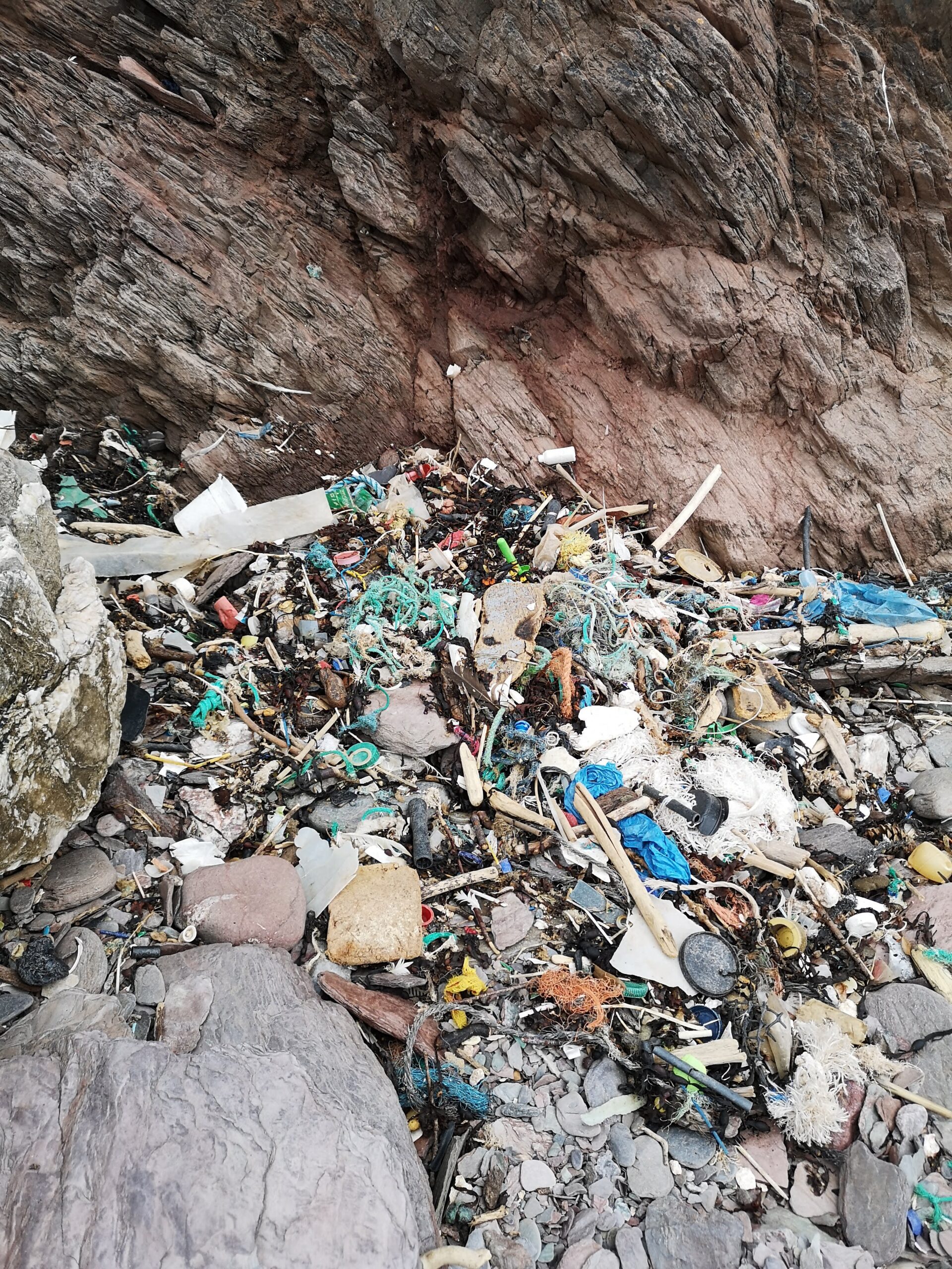 an image showing lots of pieces of plastic and litter on the beach between rocks
