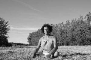 Photo of Asher sat in the field, alone and smiling at the camera