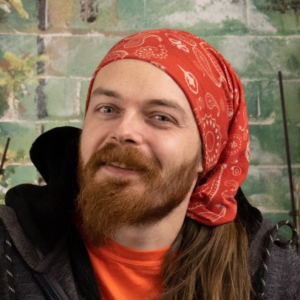 Portrait of Joe smiling, wearing a red bandana and orange shirt.