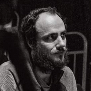 Black and white portrait of Tick, looking slightly to the side, with short hair and a beard.