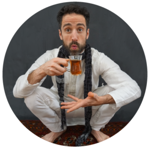 Bobak, squatting on a prayer rug, holding herbal tea while blowing on it, looking at camera.