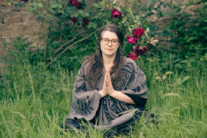 Sophie seated in the grass with hands together, wearing glasses and a patterned shawl.