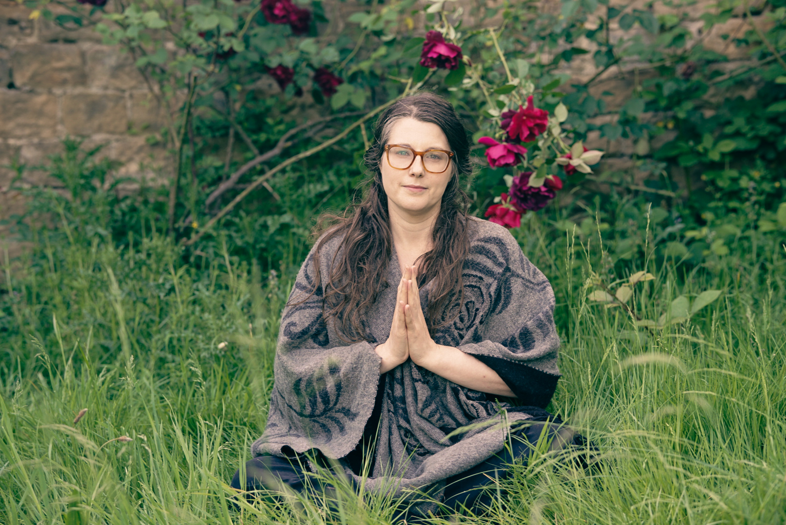 Sophie seated in the grass with hands together, wearing glasses and a patterned shawl.