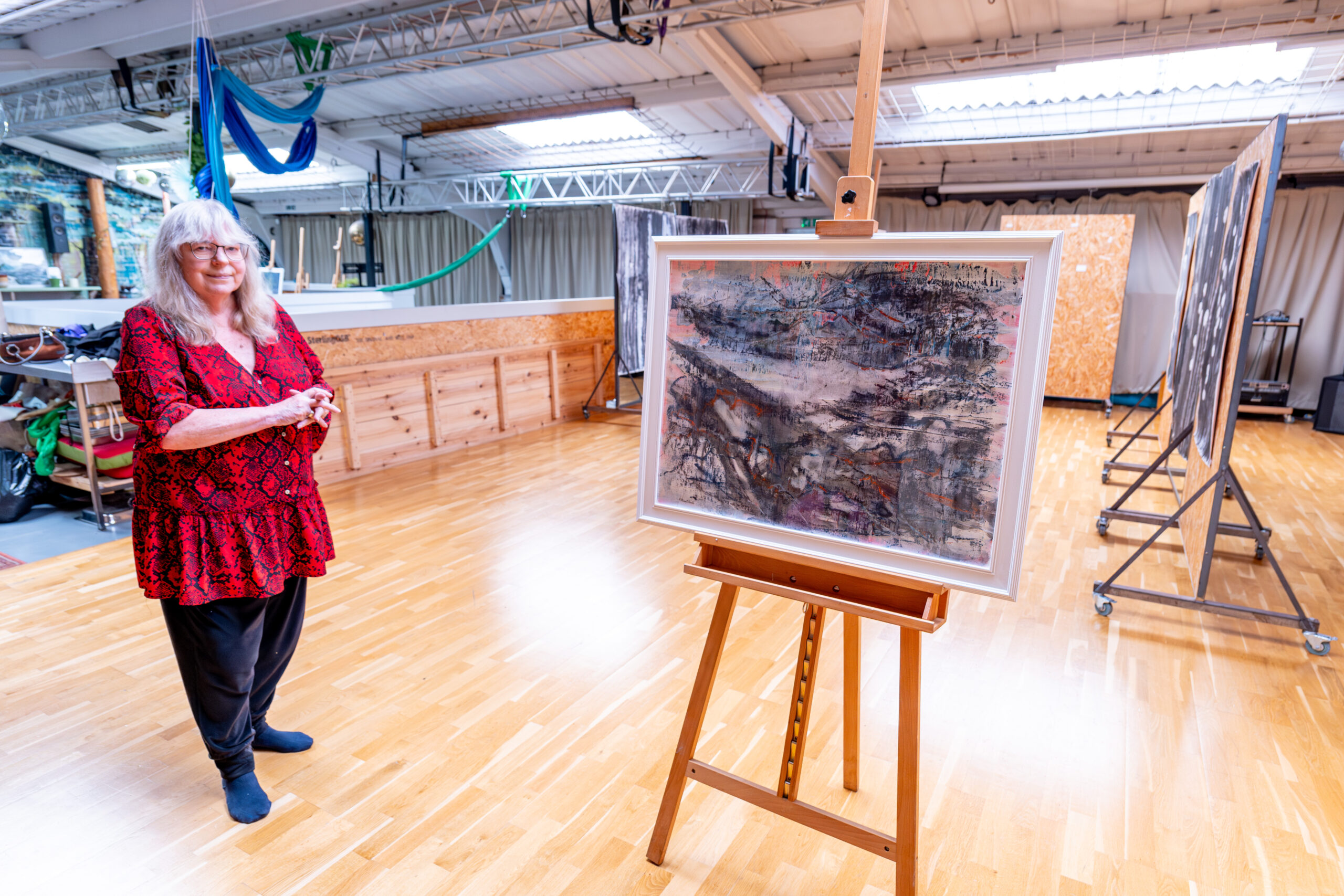 Alison stood next to one of her watercolour painting, on a easel. Standing in Open SOurce Arts, displaying her artwork around her, during her exhibition