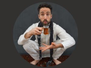 Bobak squats barefoot dressed all in white, holding a glass of tea