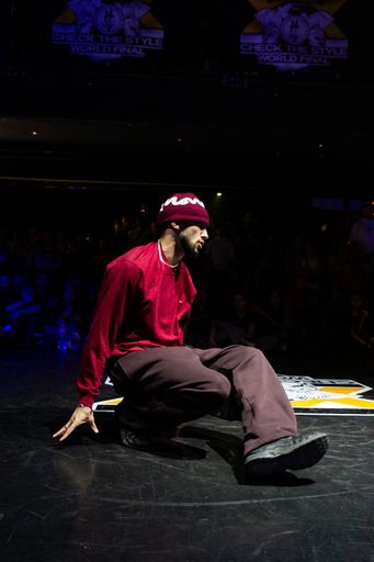Kieron who is performing breaking with a floor move in a red outfit under stage lights.